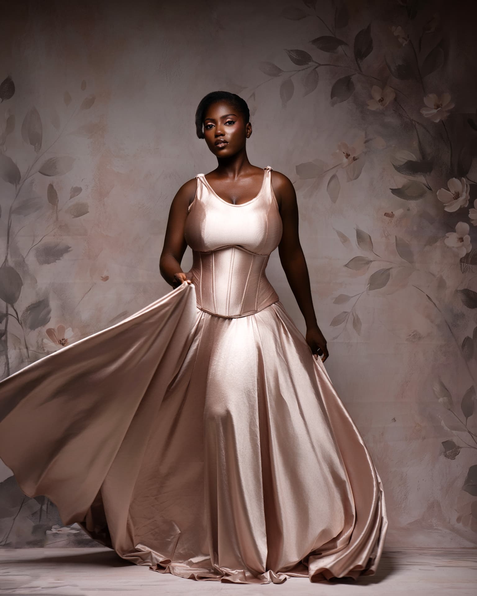Studio portrait in a flowing rose satin gown against a floral backdrop